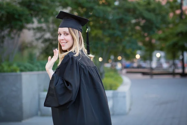 Female student waving hand at graduation on college campus Royalty Free Stock Images