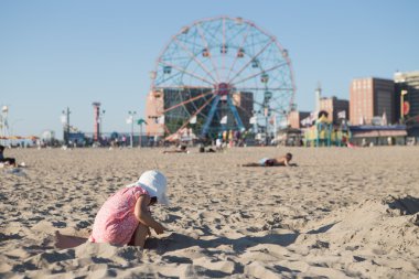 Küçük kız kumsalda kumla oynuyor.