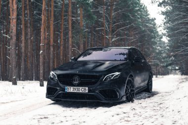 Kherson, Ukrayna - Şubat 2021. Güçlü Mercedes-AMG E63 S Brabus Kışın karlı ormanda mat siyah renkte.