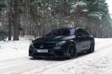 Kherson, Ukrayna - Şubat 2021. Güçlü Mercedes-AMG E63 S Brabus Kışın karlı ormanda mat siyah renkte.