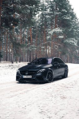 Kherson, Ukrayna - Şubat 2021. Güçlü Mercedes-AMG E63 S Brabus Kışın karlı ormanda mat siyah renkte.