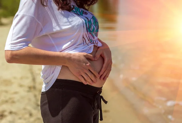 pregnant woman touches her belly hands making a heart on the bea