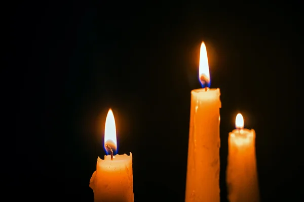 Три палаючі воскові свічки на чорному тлі — стокове фото