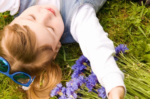 Menina deitada na grama com flores — Fotografia de Stock