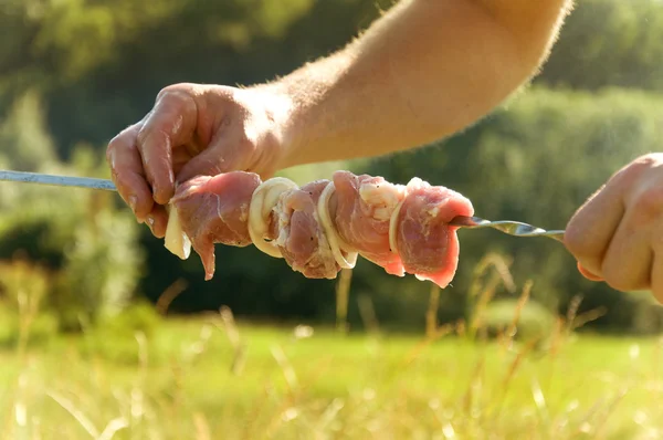 Hombre encadenando la carne en un pincho Imagen de archivo