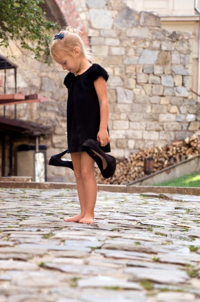 Little girl holding her shoes and stands barefoot on the road — Stock Photo, Image