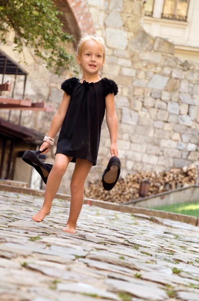 Little girl carries a shoes and goes barefoot on the road — Stock Photo, Image