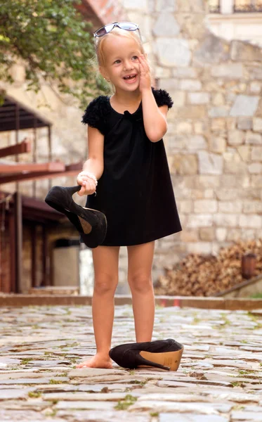 Little girl holding her shoes and stands barefoot on a road — Stock Photo, Image