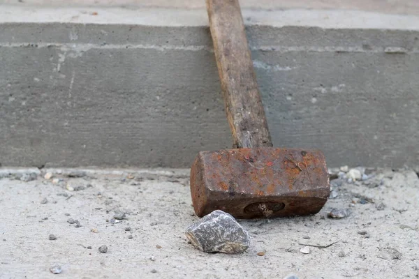Rusty iron sledgehammer with a wooden handle and a stone, on a background of gray concrete.