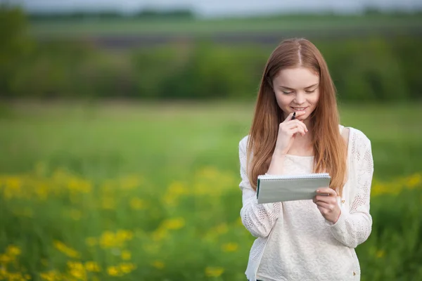 Gelukkig meisje Europees uiterlijk staande op het gras met de notebook en pen — Stockfoto