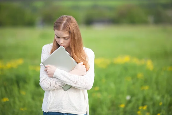 Gelukkig meisje Europees uiterlijk staande op het gras met een laptop op groene natuur achtergrond — Stockfoto