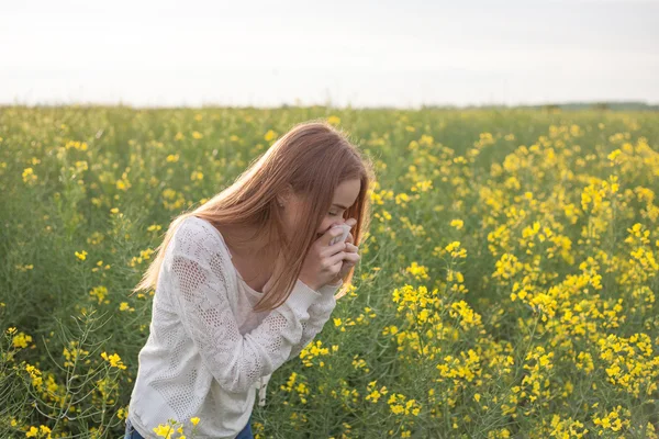 Pollen allergi, pige nysen i en rapsfrø felt af blomster - Stock-foto