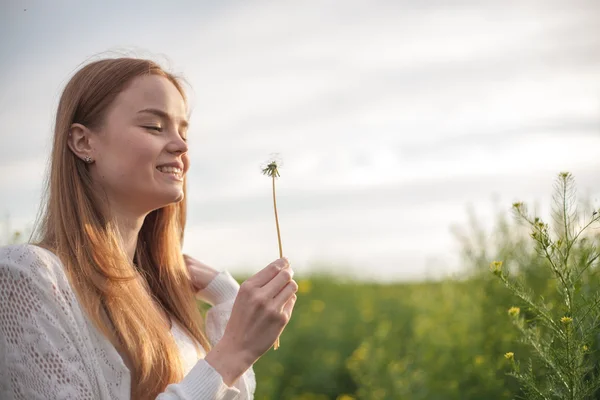 Junge Frühlingsmode-Frau bläst Löwenzahn im Frühlingsgarten. Frühling. Trendiges Mädchen bei Sonnenuntergang im Frühling Landschaft Hintergrund. Allergisch gegen Blütenpollen. Frühlingsallergie. — Stockfoto