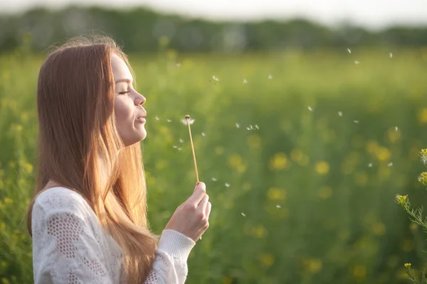 Junge Frühlingsmode-Frau bläst Löwenzahn im Frühlingsgarten. Frühling. Trendiges Mädchen bei Sonnenuntergang im Frühling Landschaft Hintergrund. Allergisch gegen Blütenpollen. Frühlingsallergie — Stockfoto