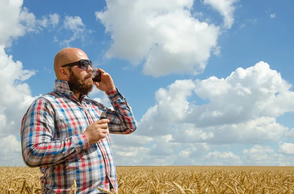 Άτριχος αγρότης στην γυαλιά στέκεται σε έναν τομέα σίτου, και μιλάμε για τηλέφωνο. — Φωτογραφία Αρχείου