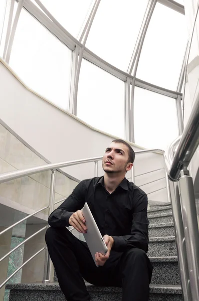 Empresário feliz sentado nas escadas com tablet digital no escritório e olhar para cima . — Fotografia de Stock