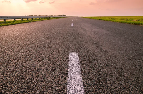 Pembe güzel gün batımı için boş asfalt yol.