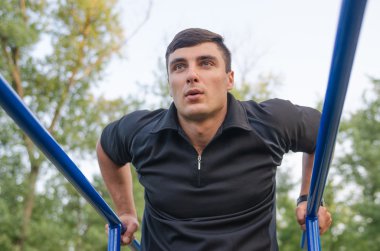 Fitness, spor, egzersiz, eğitim ve yaşam tarzı kavramı - triceps yapan genç erkek üzerinde paralel Bar açık havada daldırma.