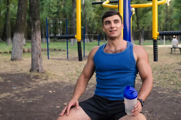 Protein ile mavi gömlekli yakışıklı sporcu görüntüsünü sallamak vasıl belgili tanımlık park spor salonu ile.