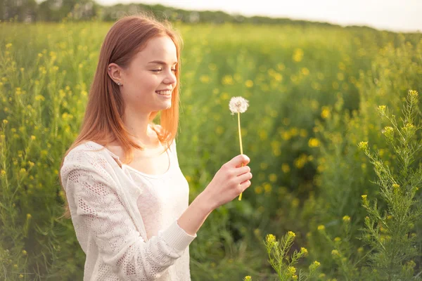 Junge Frühlingsmode Frau pustet Löwenzahn im Frühling Garten. Frühling. trendiges Mädchen bei Sonnenuntergang im Frühling Landschaft Hintergrund — Stockfoto