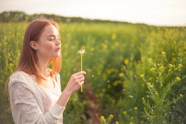 Junge Frühlingsmode Frau pustet Löwenzahn im Frühling Garten. Frühling. trendiges Mädchen bei Sonnenuntergang im Frühling Landschaft Hintergrund — Stockfoto