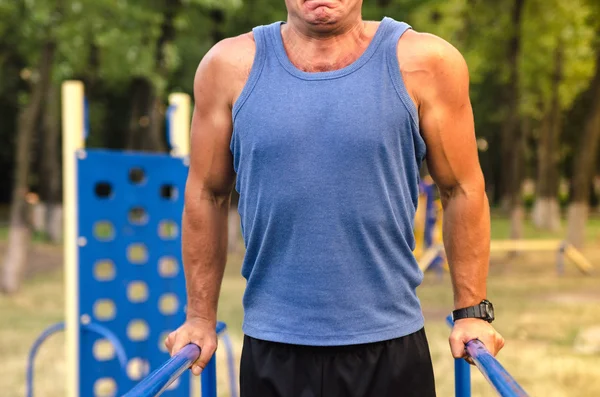 Fitness, deporte, ejercicio, entrenamiento y concepto de estilo de vida: un joven irreconocible que se sumerge en tríceps en bares paralelos al aire libre . — Foto de Stock