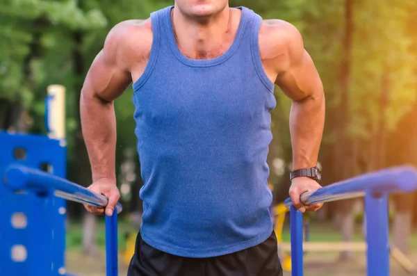 Fitness, deporte, ejercicio, entrenamiento y concepto de estilo de vida: un joven irreconocible que se sumerge en tríceps en bares paralelos al aire libre . — Foto de Stock