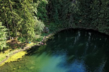 Aerial view of few people swimming in crystal clear lake in the deep forest in summer