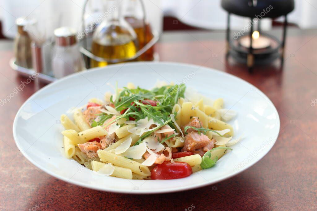 Restaurant food with fresh ingredients - pasta with tomatoes, salmon, parmesan and fresh rucola