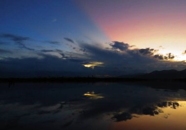 Pembe ve mavi gökyüzü öğleden sonra sakin göle yansıyor.