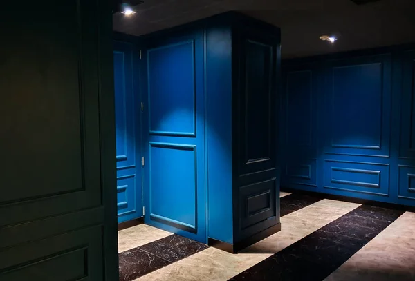 Blue doors contrast with strong shadows and lights on black and white striped floor.