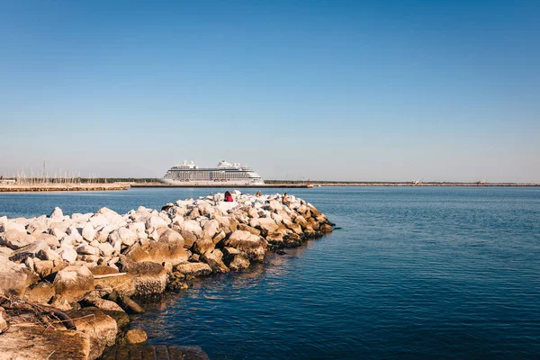 Marina di Ravenna, Emilia Romagna - İtalya - Ağustos 2020: Arka planda yolcu gemisi olan insanlarla kayalar