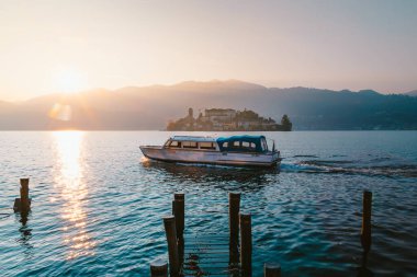 Orta San Giulio, İtalya - Aralık 2020: Orta Gölü 'ndeki San Giulio adasının gün batımında göle açılacak turist teknesiyle görüntüsü