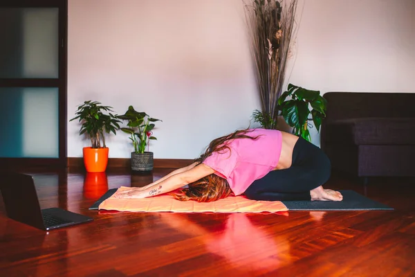 Evinin oturma odasında fiziksel egzersiz (gerinme, yoga) yapan genç bir kadın.