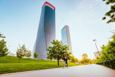 Milan, İtalya - Mayıs 2021: Arka planda modern gökdelenlerle Milano 'daki Şehir Hayatı Bölgesi Parkı' nda yürüyen kişi