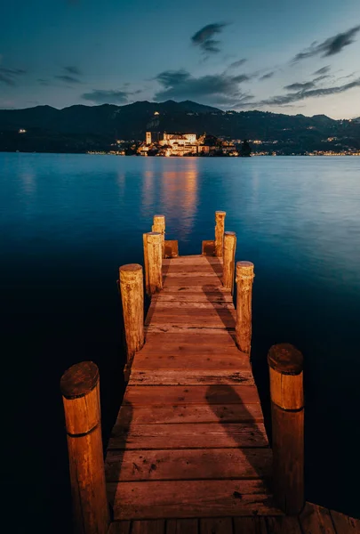 Orta San Giulio / İtalya - Haziran 2021: San Giulio adası, günbatımında ön planda ahşap bir iskele (mavi saat), uzun pozlama