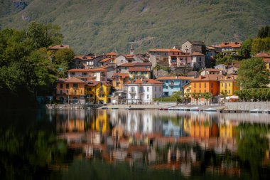 Mergozzo, Piedmont, İtalya - 3 Mayıs 2024: Mergozzo 'nun geleneksel evleri, Kuzey İtalya' nın cazibesini gösteren açık mavi göl suyuna yansıdı.