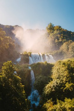 Marmore, İtalya - 19 Ağustos 2025: Parlak yaz ışığında yoğun yeşil bitki ve orman bitkileri tarafından çerçevelenen şelale.