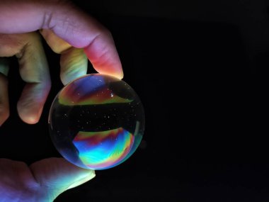 Siyah arka planda üç parmağı izole bir şekilde kristal küreyi yakan renkli bir el..