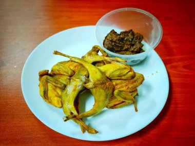 Zerdeçal tozunda kızarmış bıldırcın ve ahşap masadaki beyaz tabağın içinde sığır eti rendang..