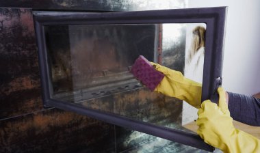 Sarı eldivenli bir kadın şöminenin camını yıkıyor. Günlük ödev günlük kış rutini
