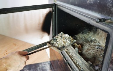 Şömine temizliği. Adam kürekle kürek tutuyor. Bir el şöminenin küllerini eski çelik bir bıçakla topluyor. Günlük kış rutini