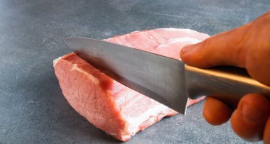 Çiğ et. Şef, gri arka planda bir bıçakla iştah açıcı bir pirzola keser..