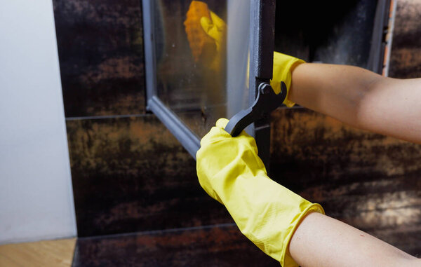 Homework. Young blonde woman in casual clothes cleans the fireplace. Close-up on the hands.
