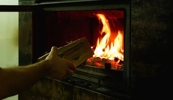 男の手は薪を暖炉の中に置く ガラスと近代的な閉じた暖炉 — ストック写真