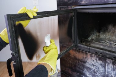 Sarı eldivenli bir kadın şöminenin camını yıkıyor. Günlük ödev günlük kış rutini