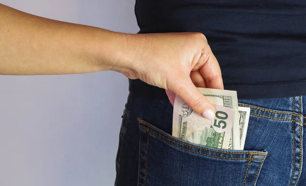 The woman pulls money out of the back pocket of the standing man\'s blue jeans. Close-up view of the hands. Place for your text.