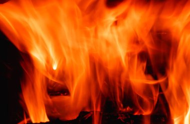 Şöminede soyut ateş alevi, arka plan dokusu. Güzel, parlak turuncu alevler gecenin karanlığında yanıp sönüyor..