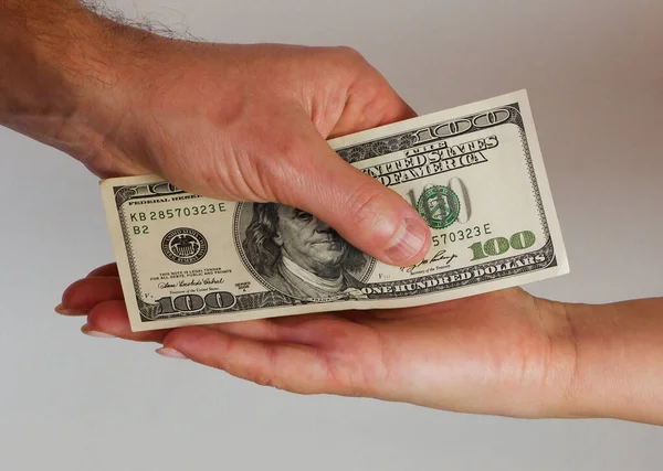 A man passes paper money American dollars to a woman. Paper money in hand. Close-up on hands on a light background.