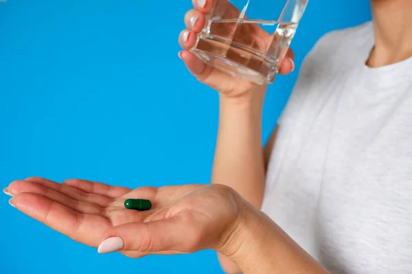 The medicine. The woman takes a pill. Tablet and glass of water in female hands on a blue background. Health care and people concept